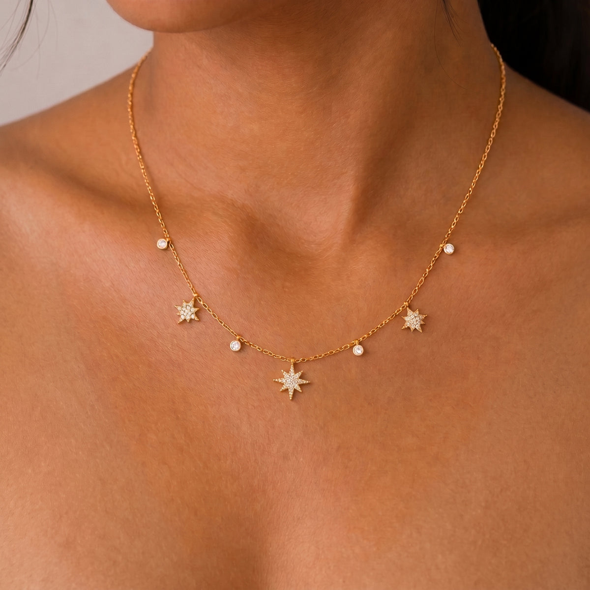 Woman wearing the Colette gold necklace with pavé star charms and tiny crystal drops at the collarbone