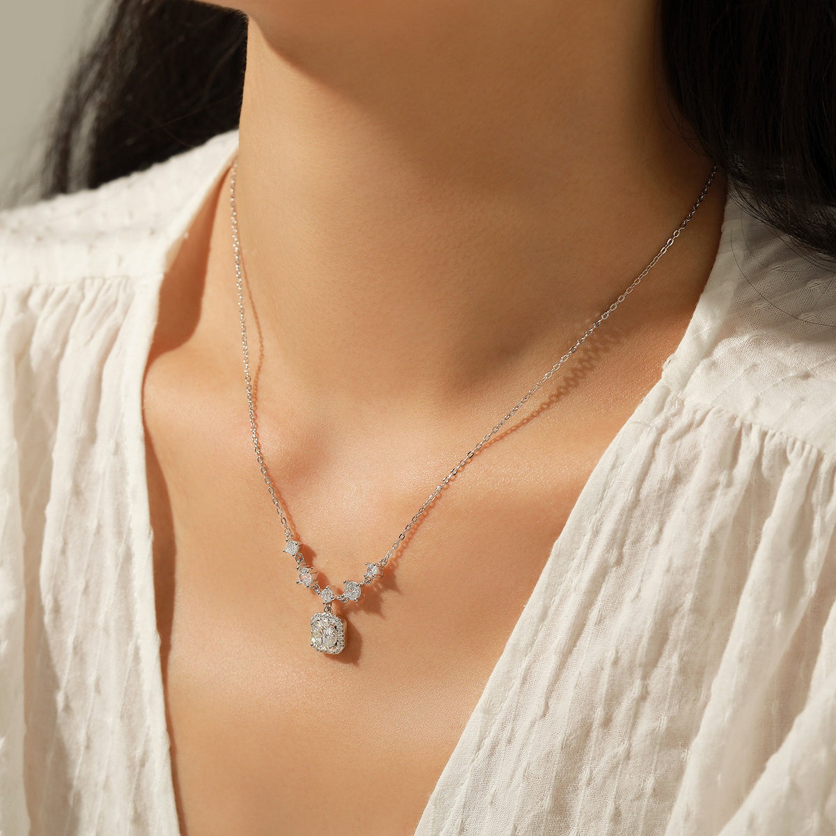 Woman in a white blouse wearing the Amélie Éclat silver necklace with a crystal cushion pendant