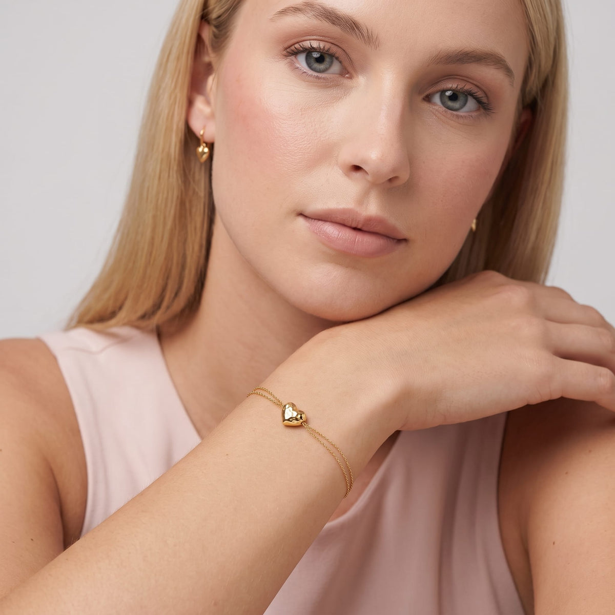 Woman wearing the Adèle hammered heart gold bracelet on the wrist while resting her chin on her hand