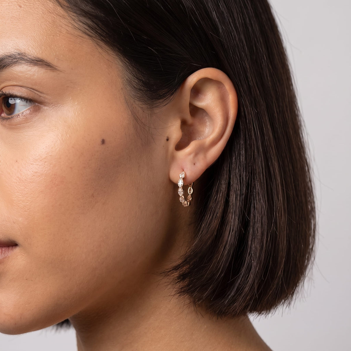 Woman wearing the Albane teardrop hoop gold earrings on the ear with short dark hair