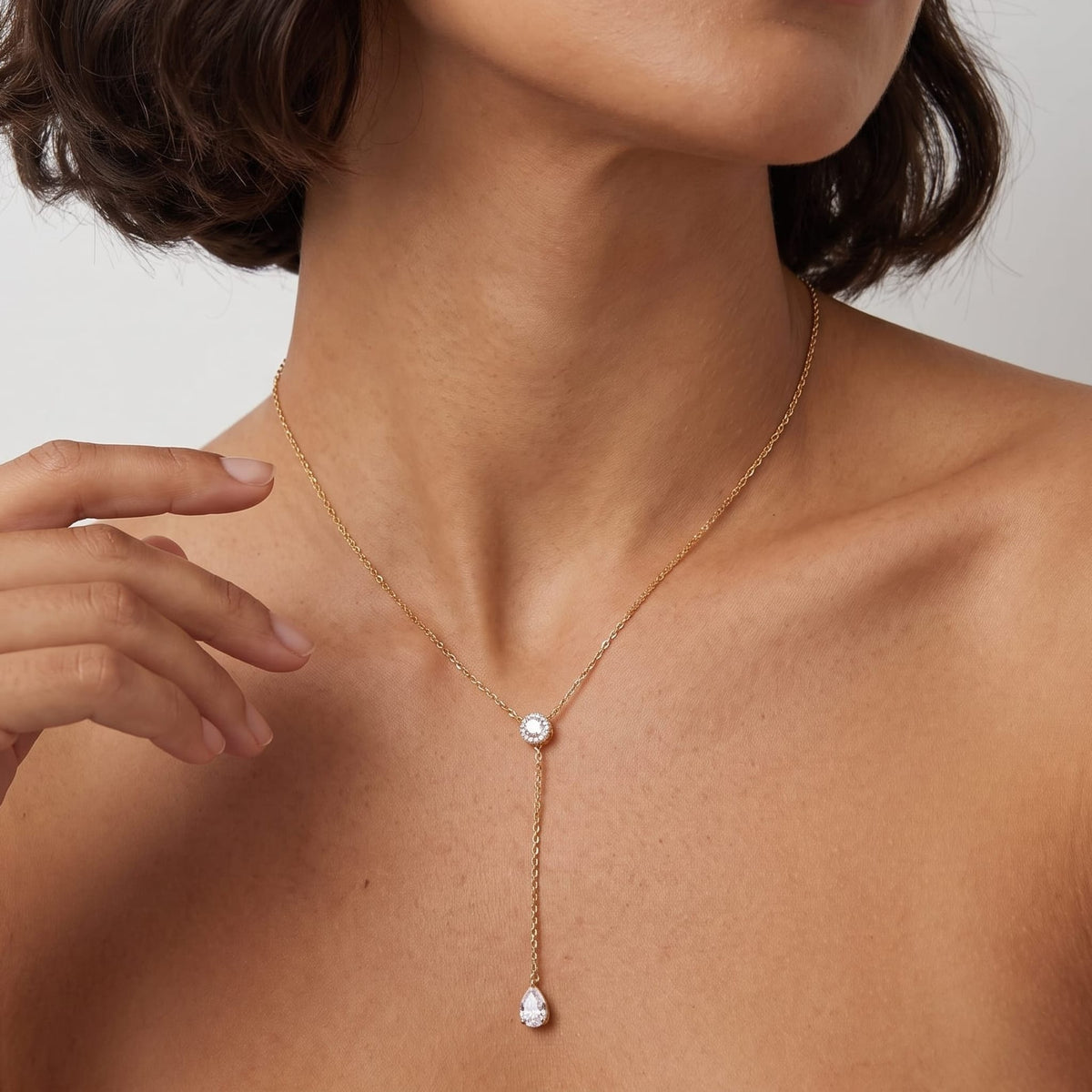 Woman wearing the Alix pear lariat gold necklace at the collarbone with short dark hair