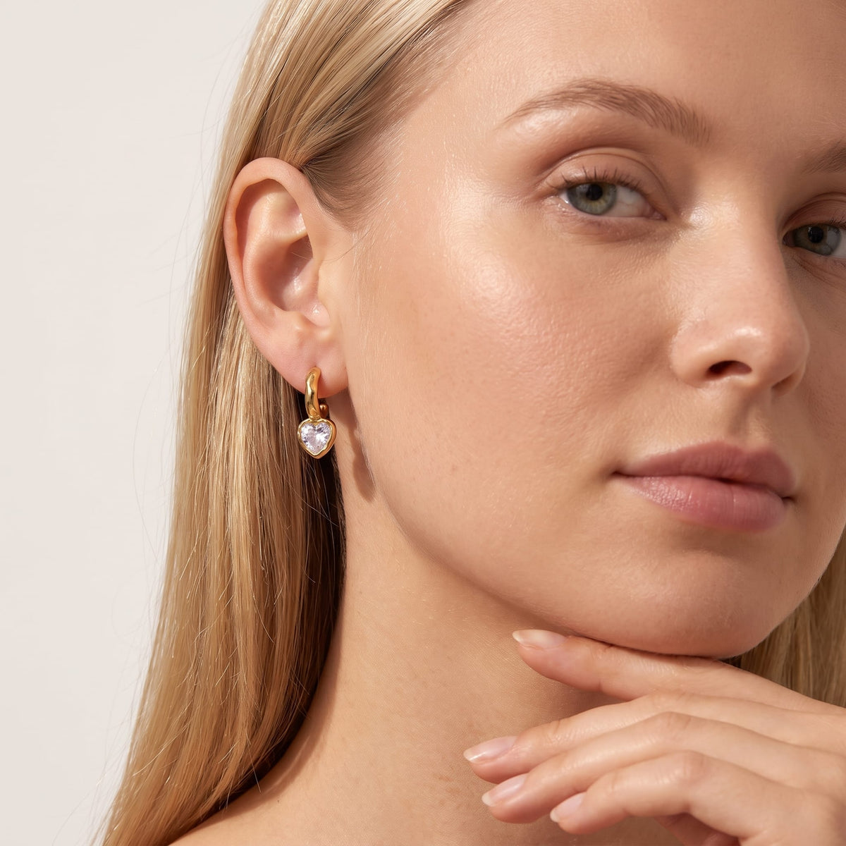 Woman wearing the Amandine hammered heart gold earrings on her ear resting her chin