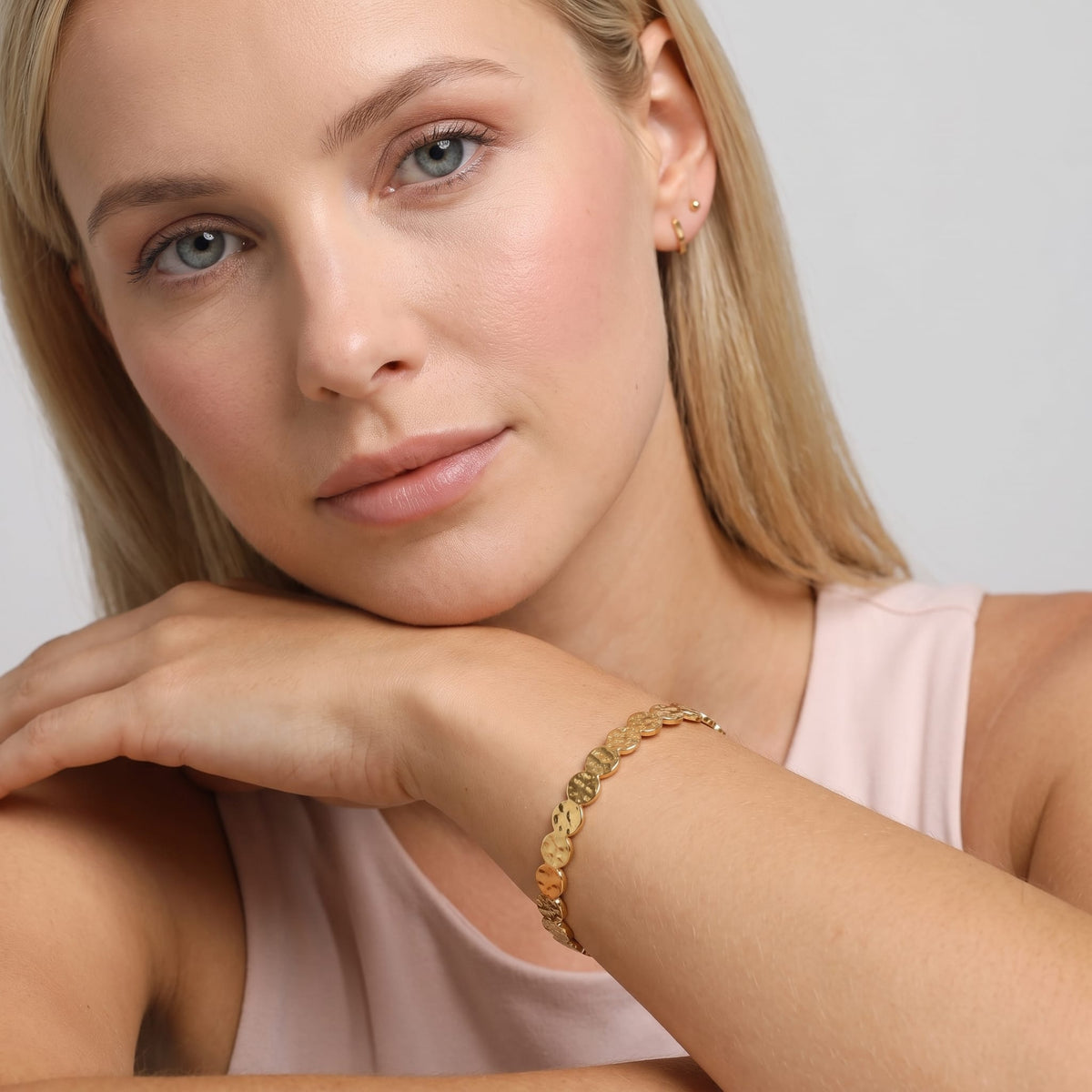 Woman wearing the Ambre hammered cuff gold bracelet on the wrist while wearing a pink top