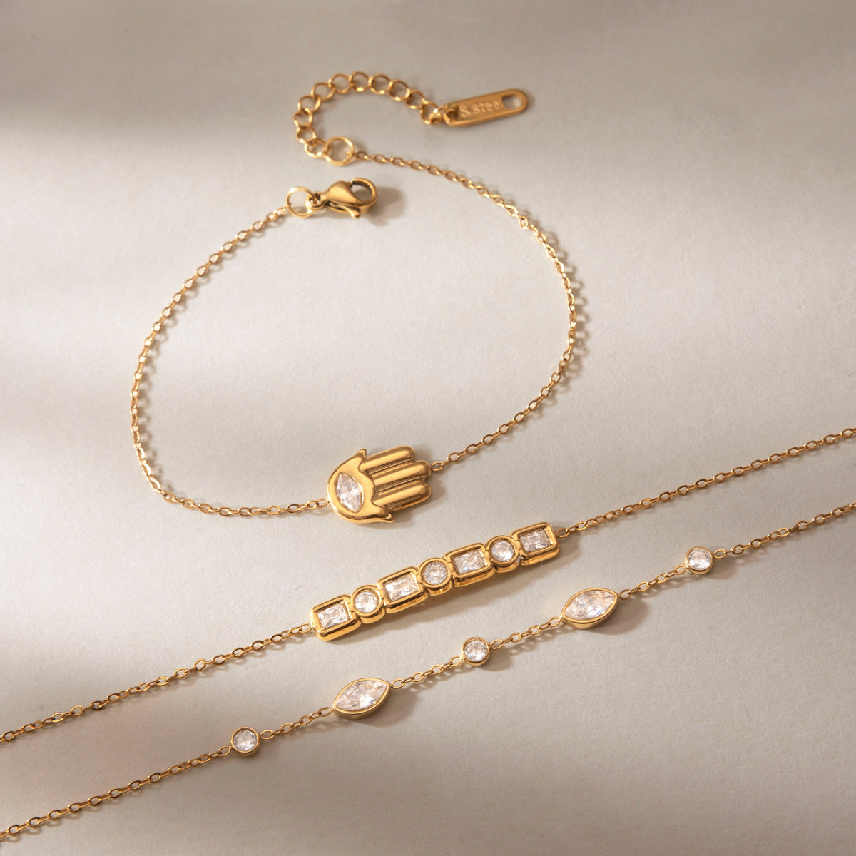 Amelia hamsa bracelet laid above a baguette bar and a marquise station bracelet on gray satin