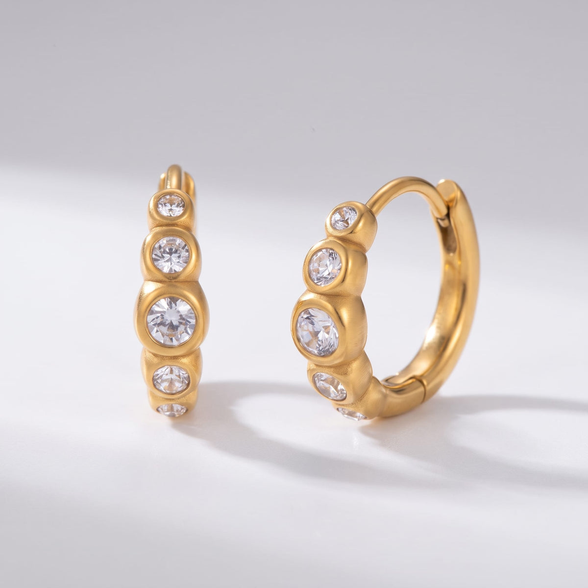 Anaïs crystal huggie gold earrings on a plain white surface casting soft shadows