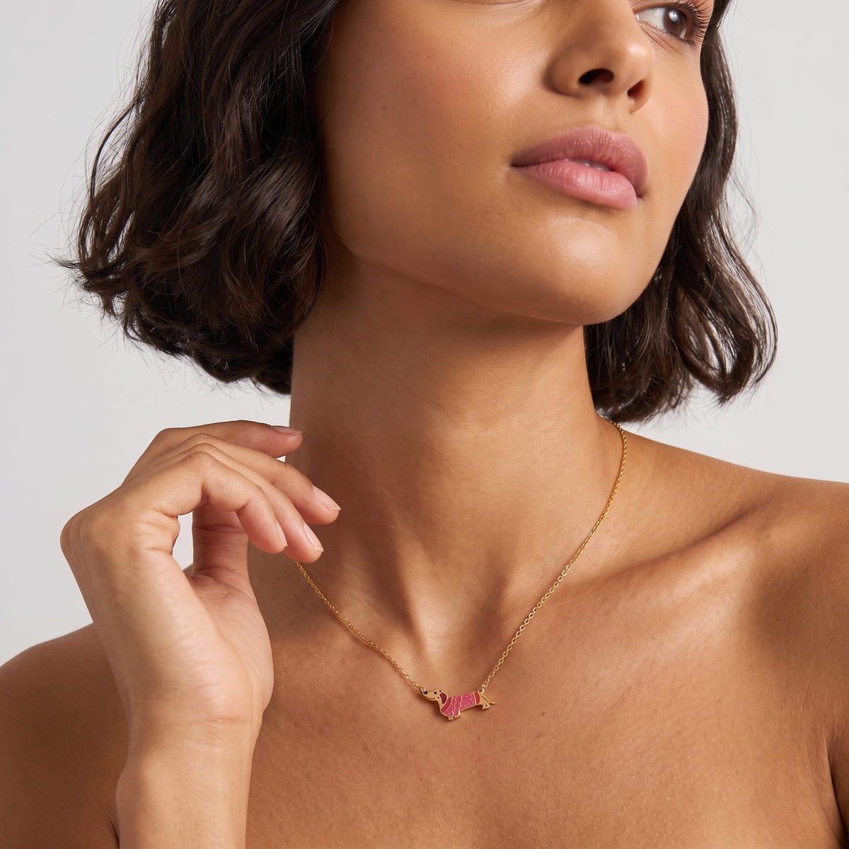 Woman wearing the Bianca pink dachshund gold necklace at the collarbone with her hand raised