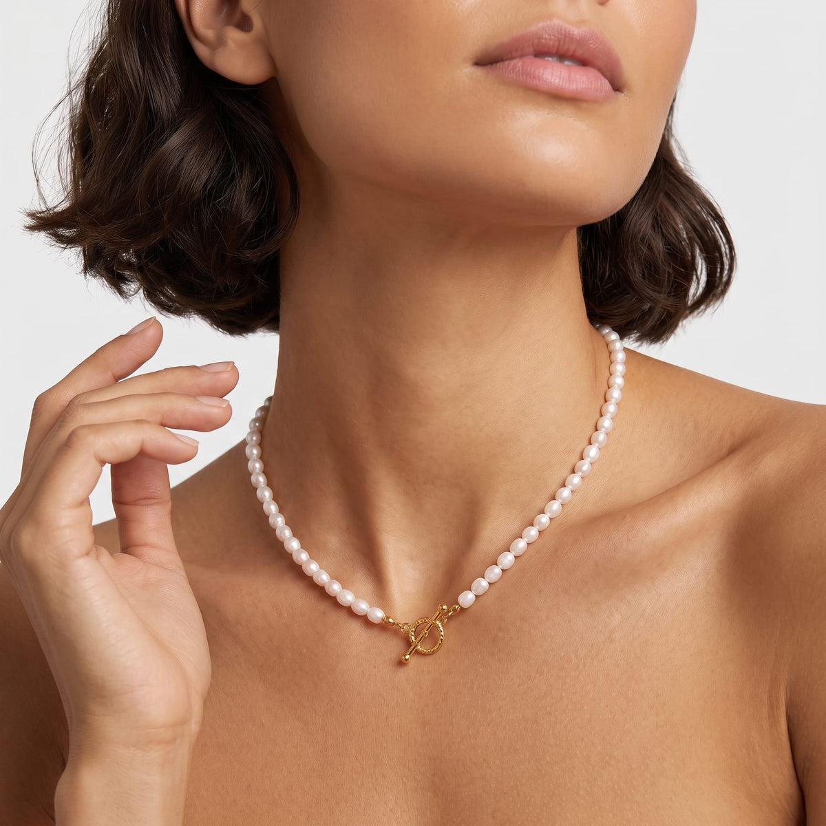 Woman wearing the Camille pearl toggle gold necklace at the throat with short dark hair
