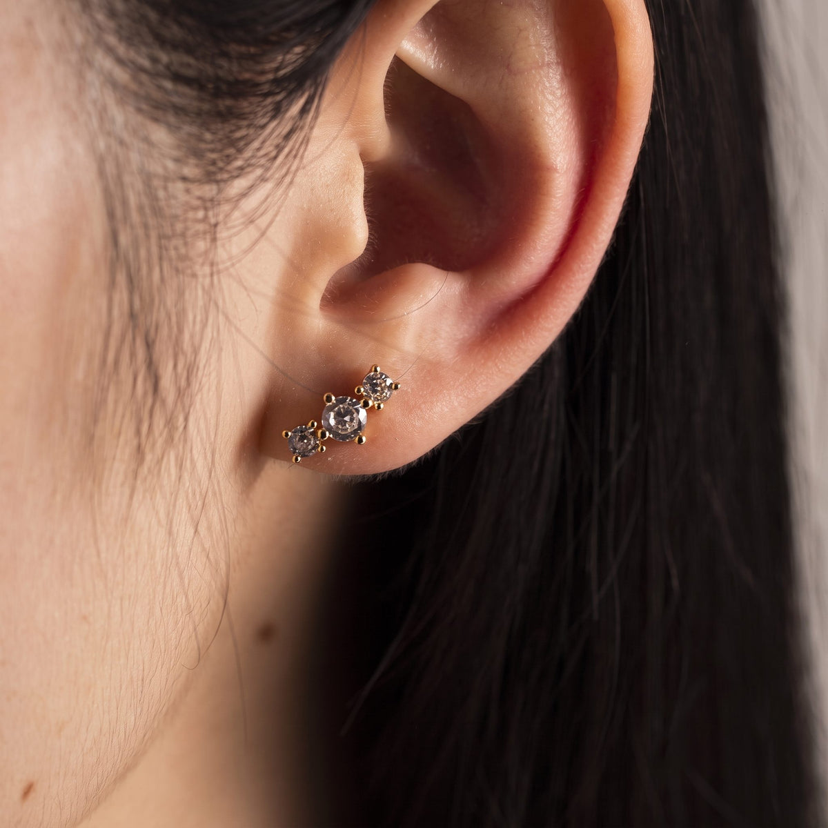 Woman wearing a Camille gold stud with three prong-set crystals climbing up from the earlobe