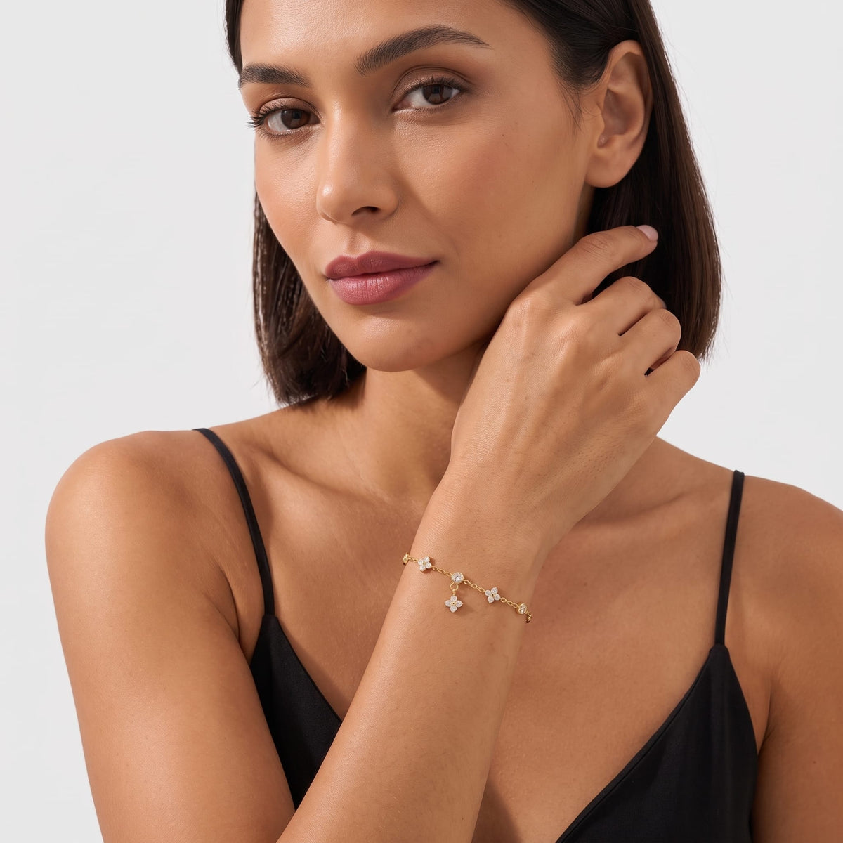 Woman wearing the Capucine clover drop gold bracelet on the wrist dressed in a black camisole