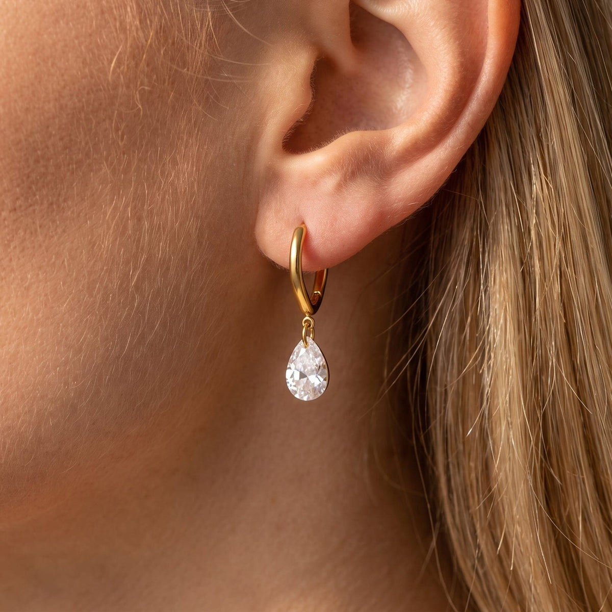 Woman wearing the Carla teardrop huggie gold earrings on the ear