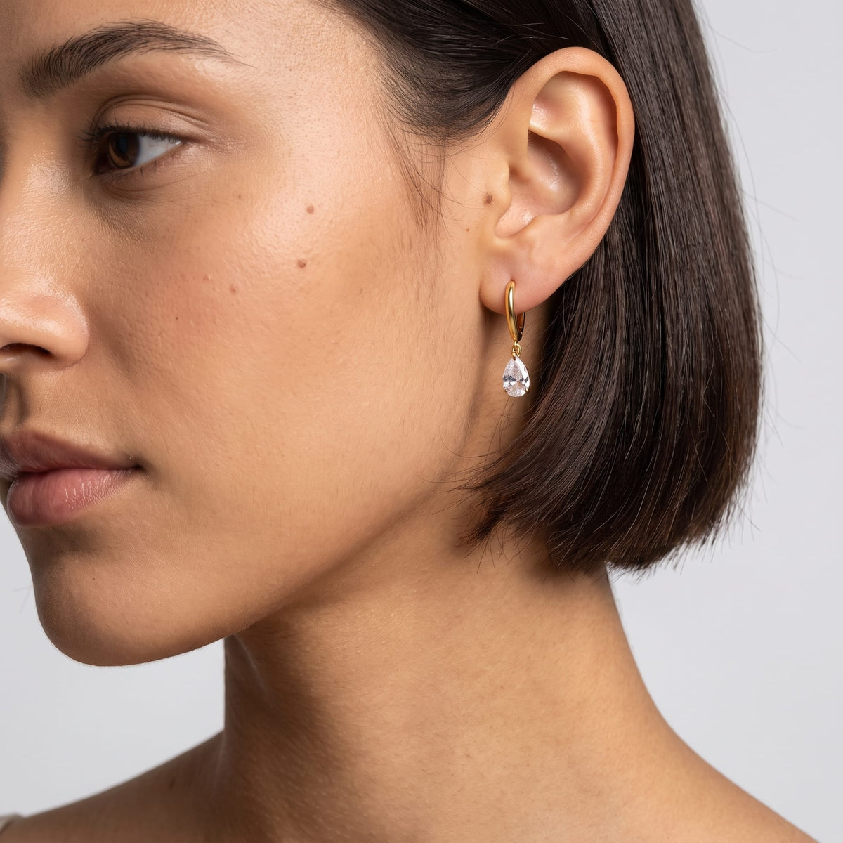 Woman wearing the Carla teardrop huggie gold earrings on the ear with dark bob haircut