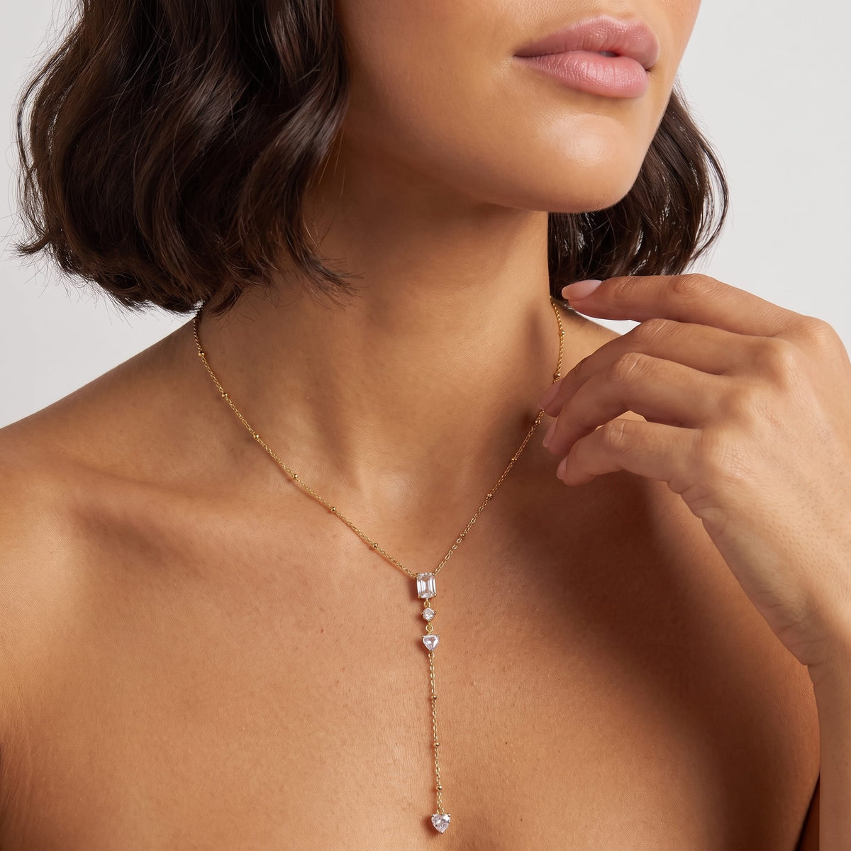 Woman wearing the Constance emerald-cut lariat gold necklace at the collarbone with her hand near her chin