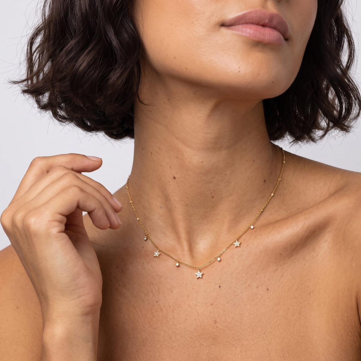 Woman wearing the Delfina crystal star gold necklace at the collarbone with her hand raised