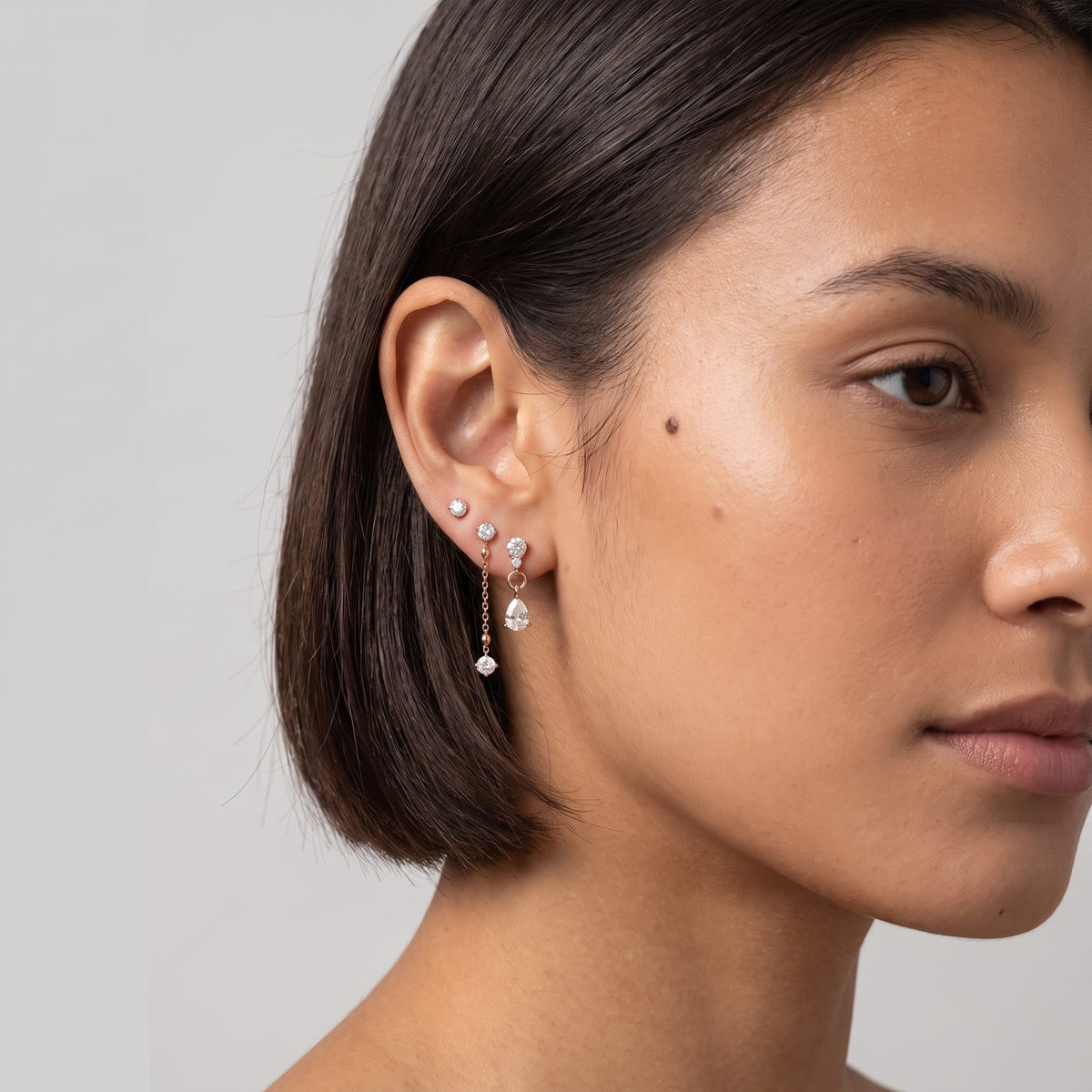 Woman wearing the Delfina drop trio gold earrings on the ear with short dark hair