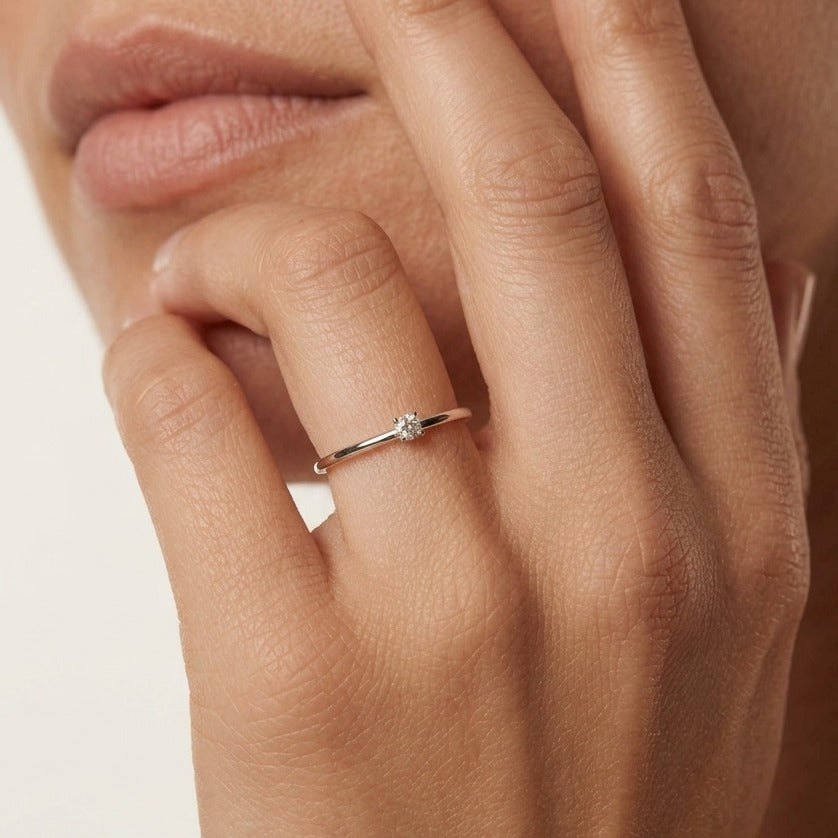 Hand at the lips wearing the Léa solo ring, a whisper-thin band with one small clear crystal