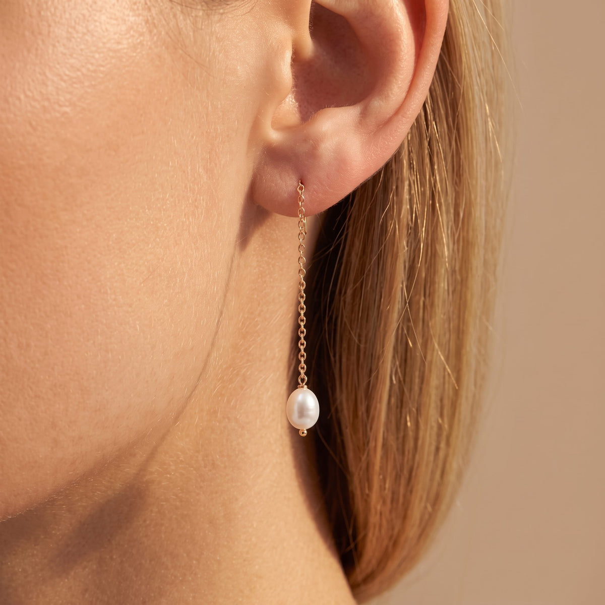 Woman wearing the Élise dainty pearl earring, a single oval pearl on a long fine gold chain