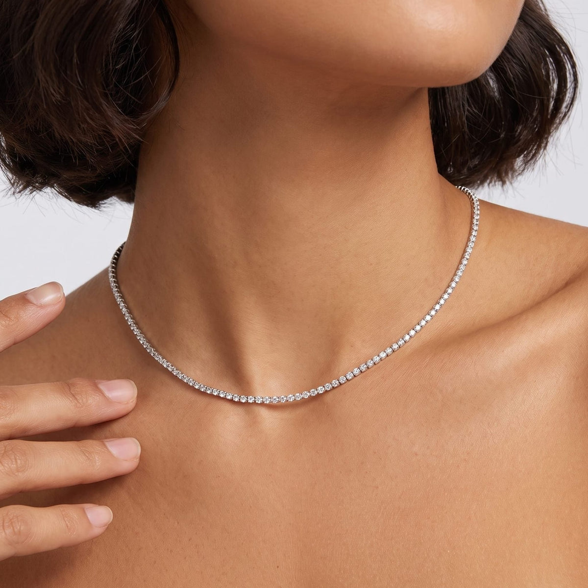 Woman with a dark bob wearing the Emma tennis chain silver necklace, one hand raised near her neck