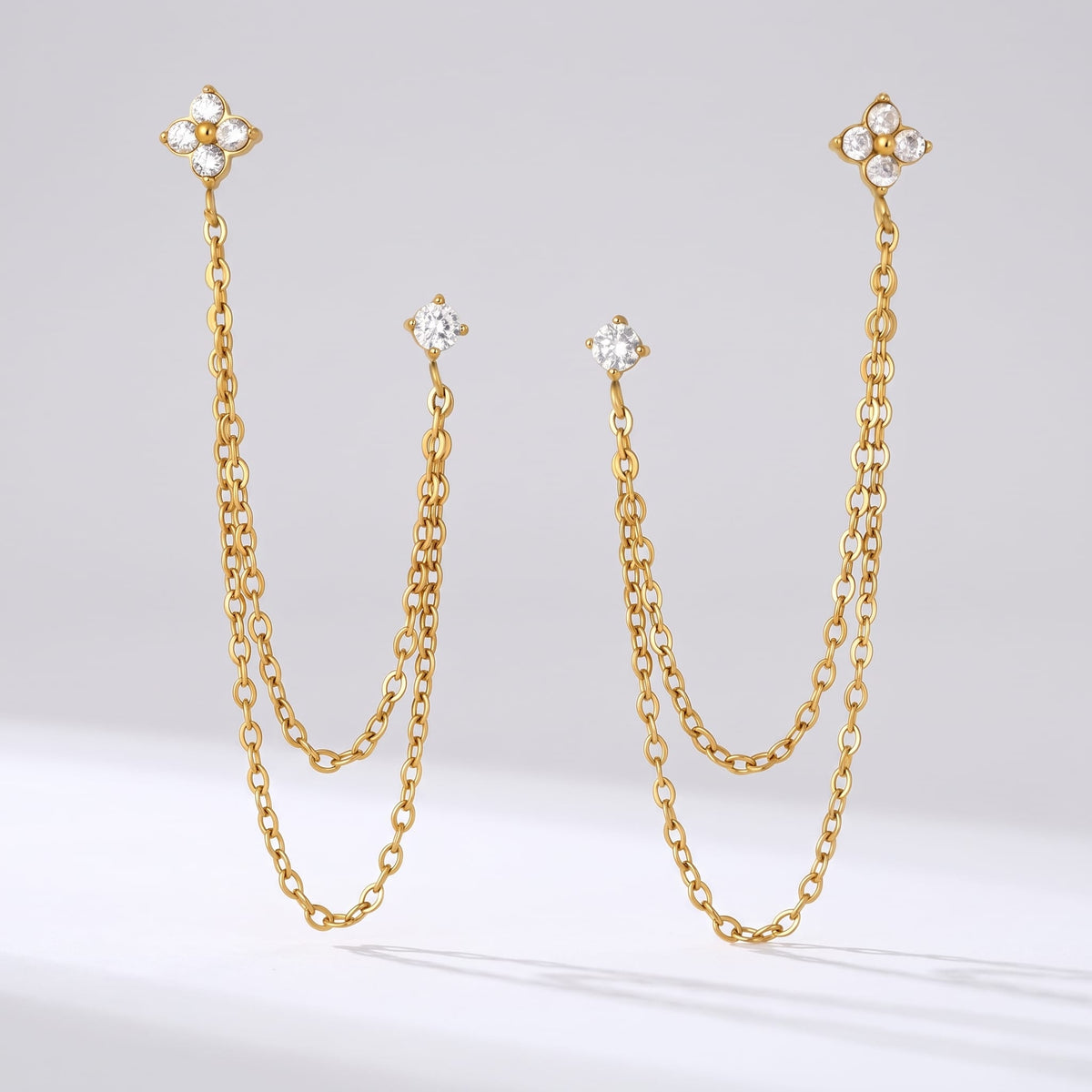 Félicie flower chain gold earrings on a plain white surface casting subtle shadows