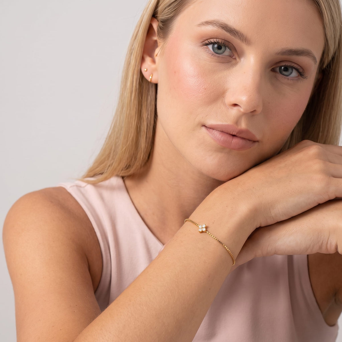 Woman wearing the Flora single clover gold bracelet on the wrist with hands rested under her chin