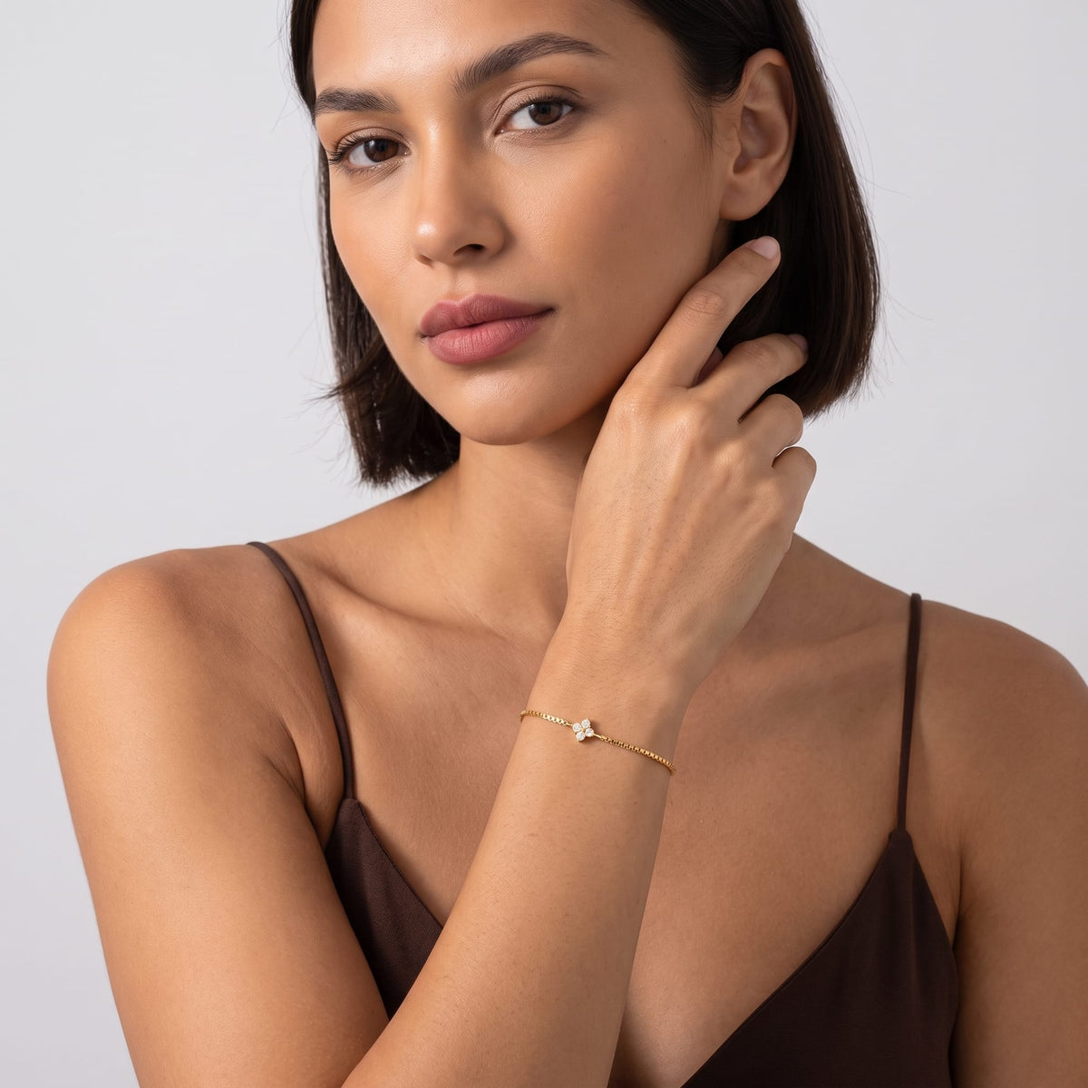 Woman wearing the Flora single clover gold bracelet on the wrist wearing a brown camisole top