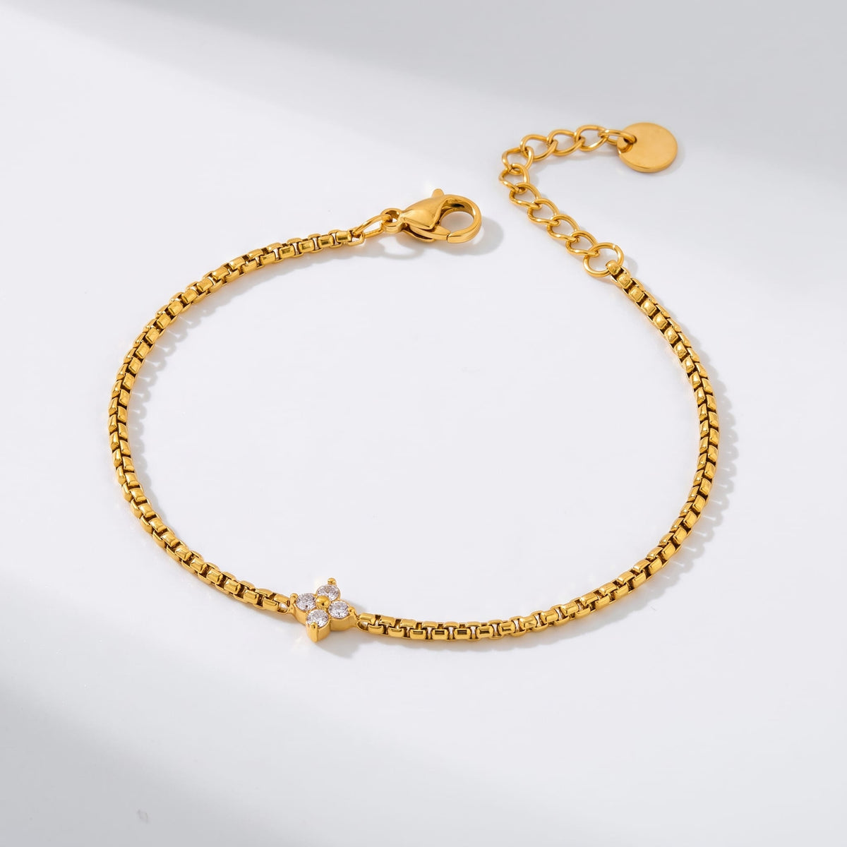 Flora single clover gold bracelet on a smooth white surface with soft shadows