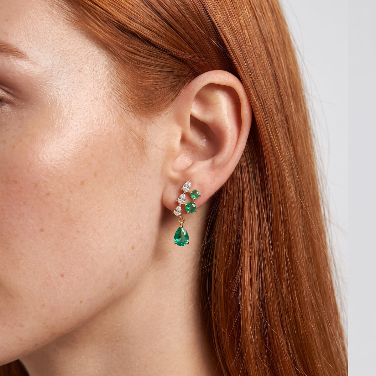 Wider view of a woman wearing the Florentine green cascade gold earrings on her ear close up with red hair