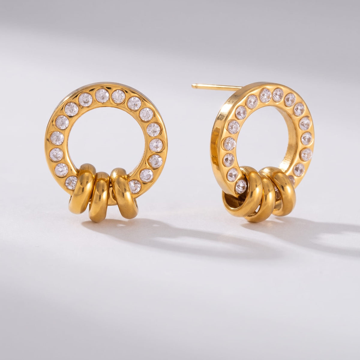 Gabrielle triple ring gold earrings on a plain white surface casting soft shadows