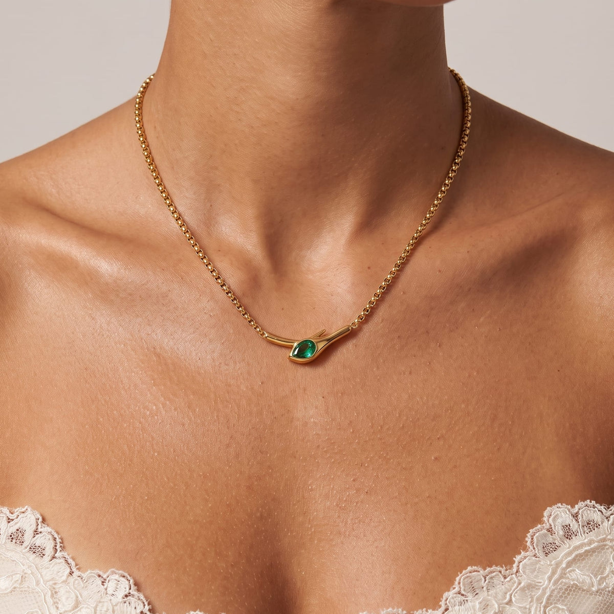 Woman wearing the Gemma green snake gold necklace at the collarbone paired with a white lace top