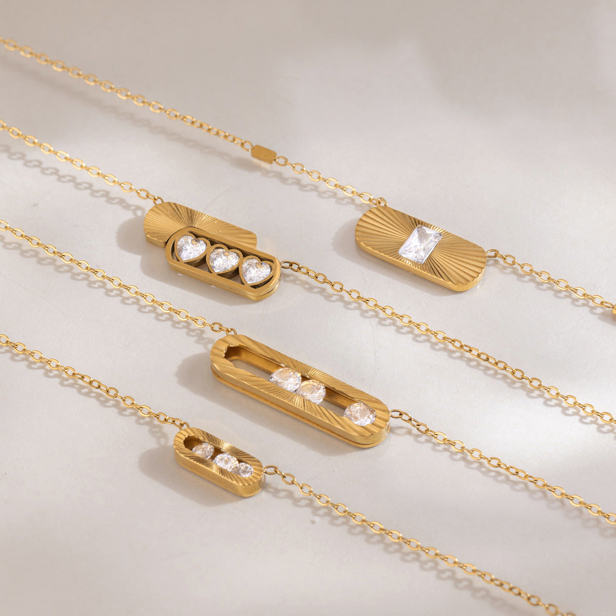 Ginevra three-heart frame over a fluted gold tab among four sunburst pendants on satin