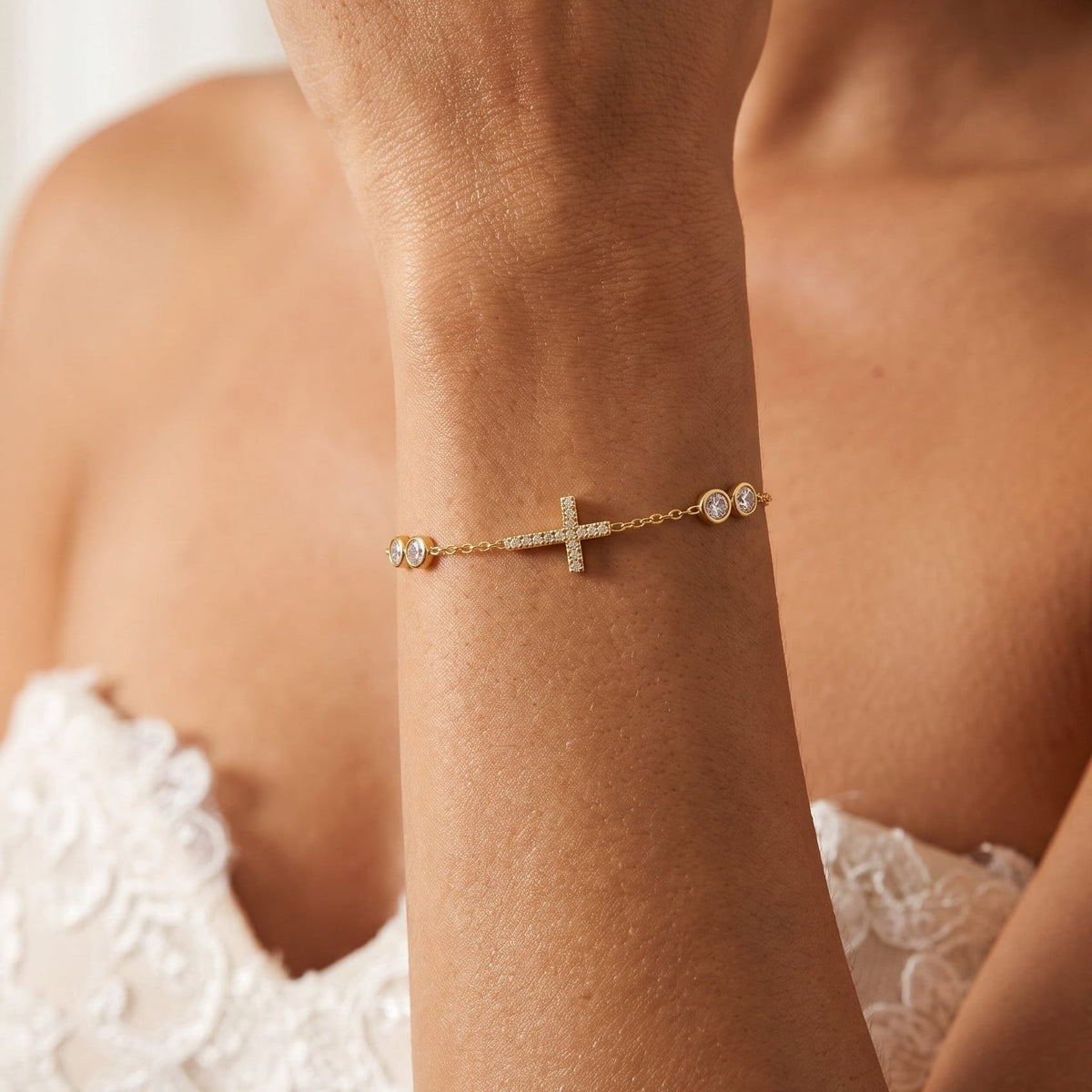 Wider view of a woman wearing the Giulia sideways cross gold bracelet on the wrist, featuring round crystals