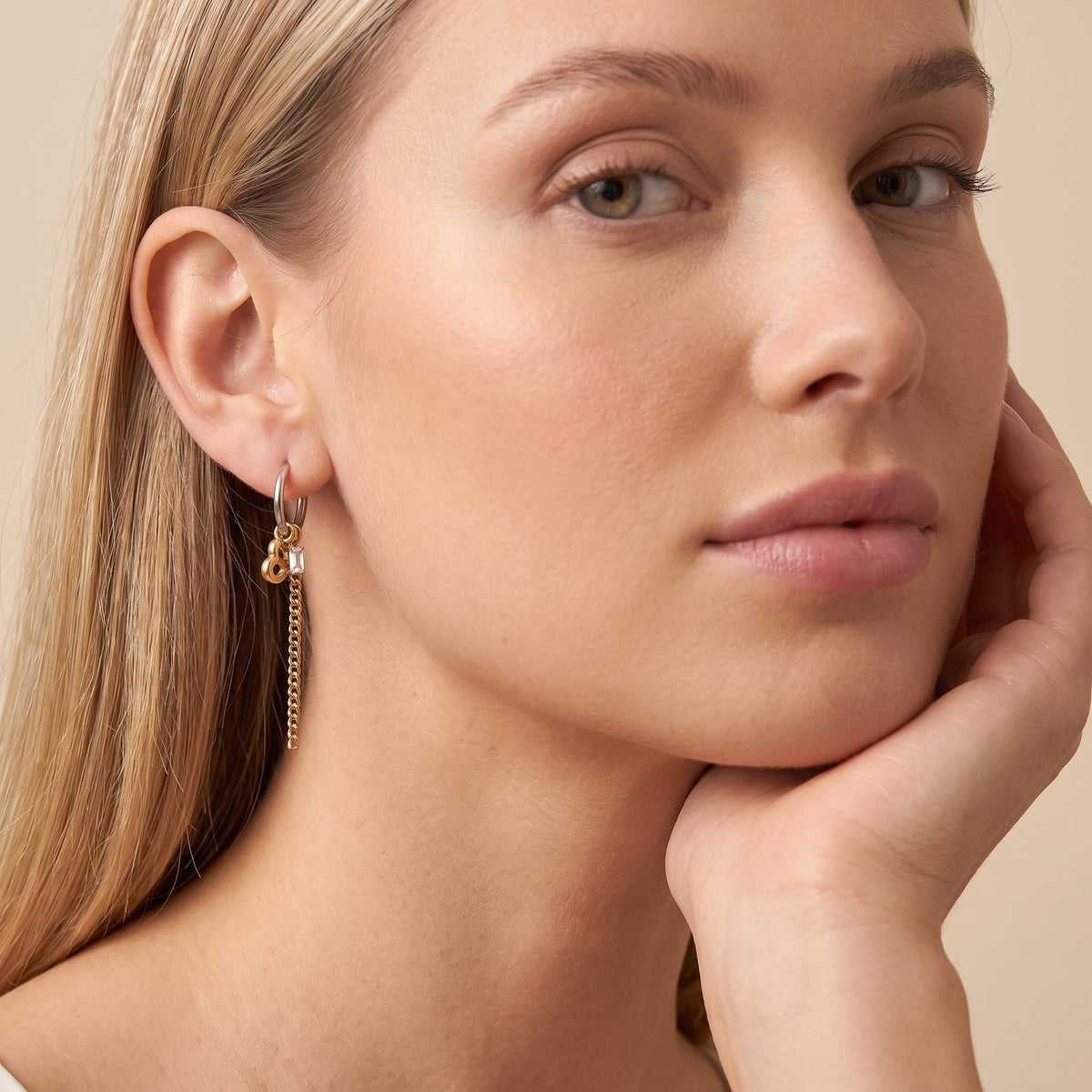 Woman wearing the Greta heart chain two-tone earrings on the ear resting chin on hand