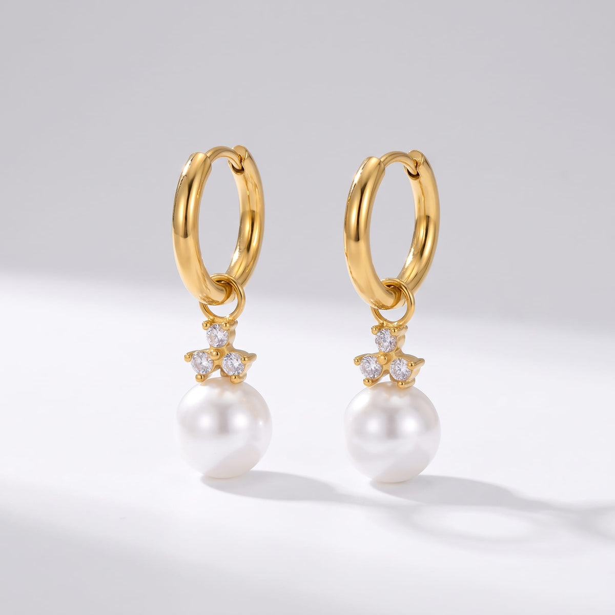 Hortense pearl huggie gold earrings on a plain white surface standing side by side