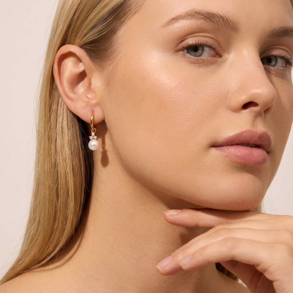 Woman wearing the Hortense pearl huggie gold earrings on her ear with hand under chin