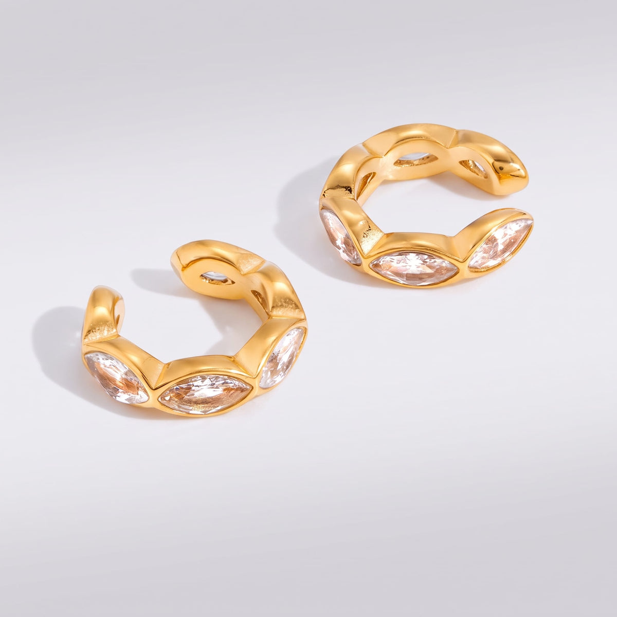 Irène marquise gold ear cuffs on a neutral surface with soft shadows