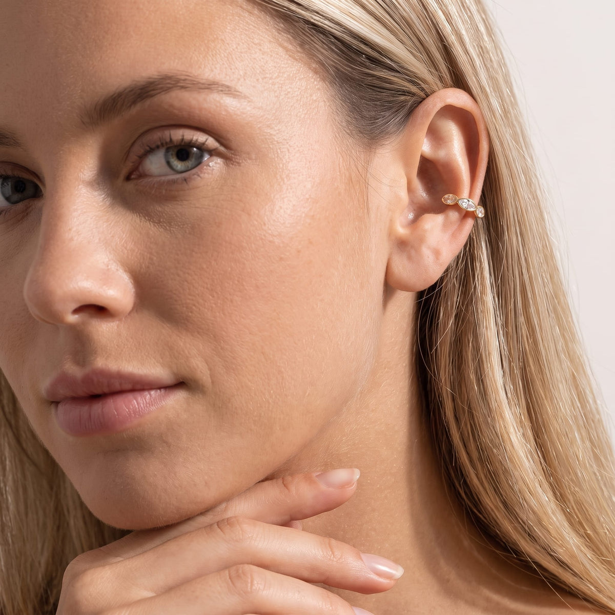 Woman wearing the Irène marquise gold ear cuffs on the ear resting her hand under her chin