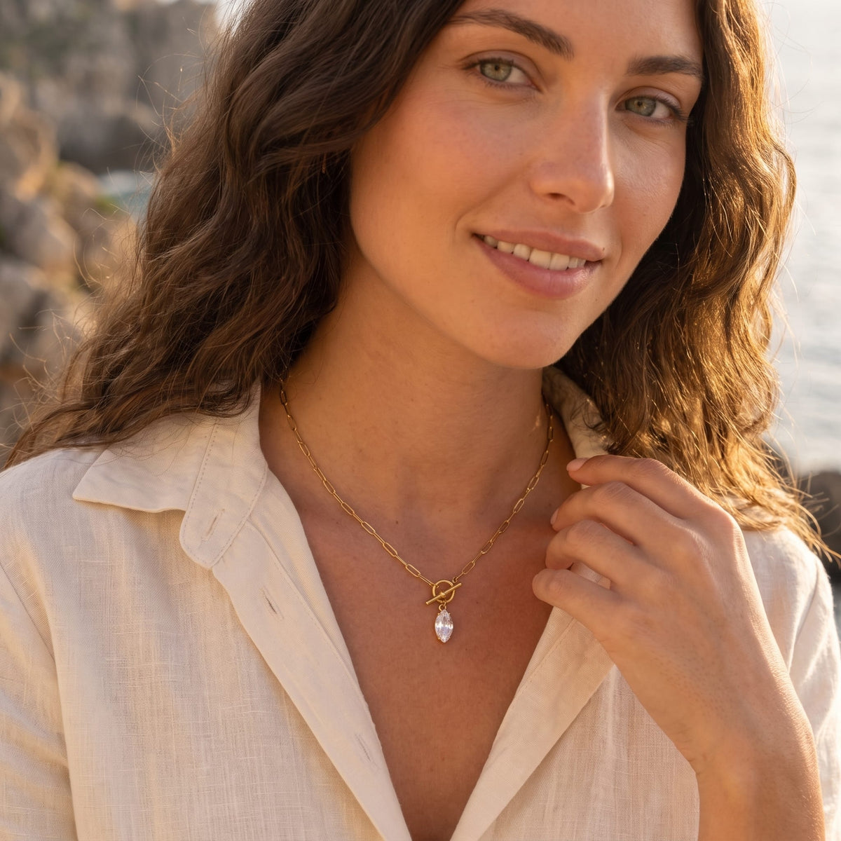 Woman wearing the Isabelle marquise toggle gold necklace at the collarbone, wearing a buttoned cream shirt