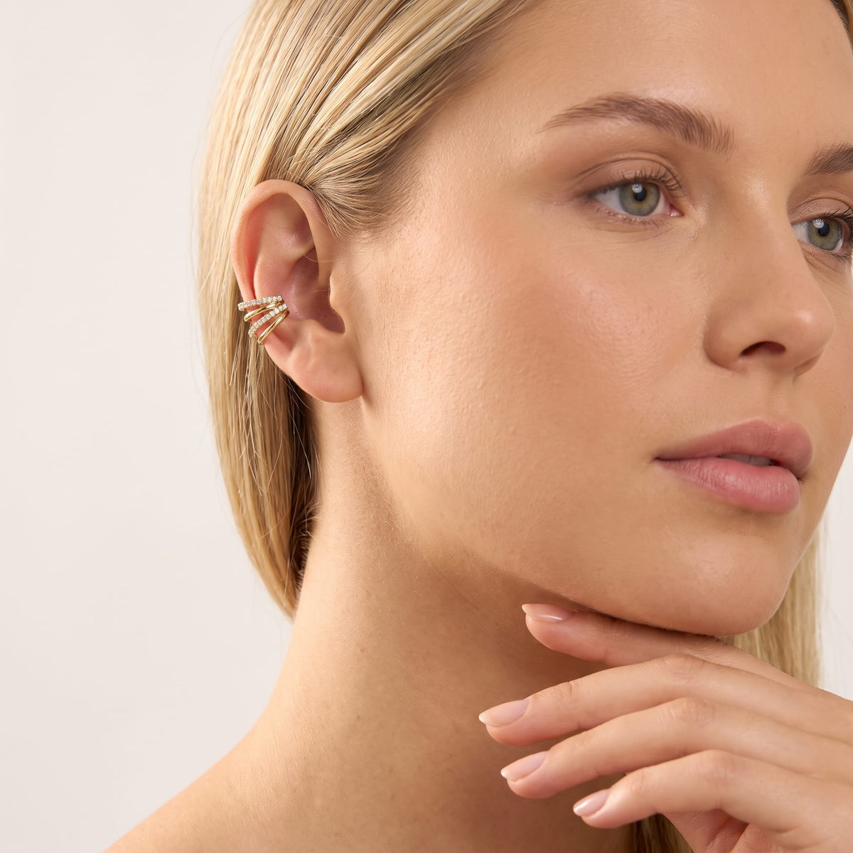 Woman wearing the Jeanne crisscross gold ear cuffs on the ear with her hand at her chin