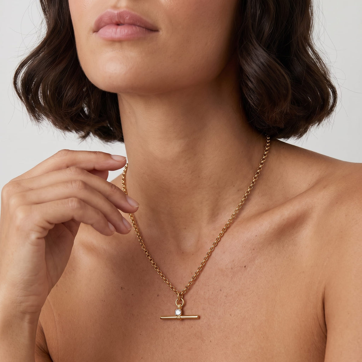 Woman wearing the Joséphine t-bar crystal gold necklace at the collarbone with her hand near her chin