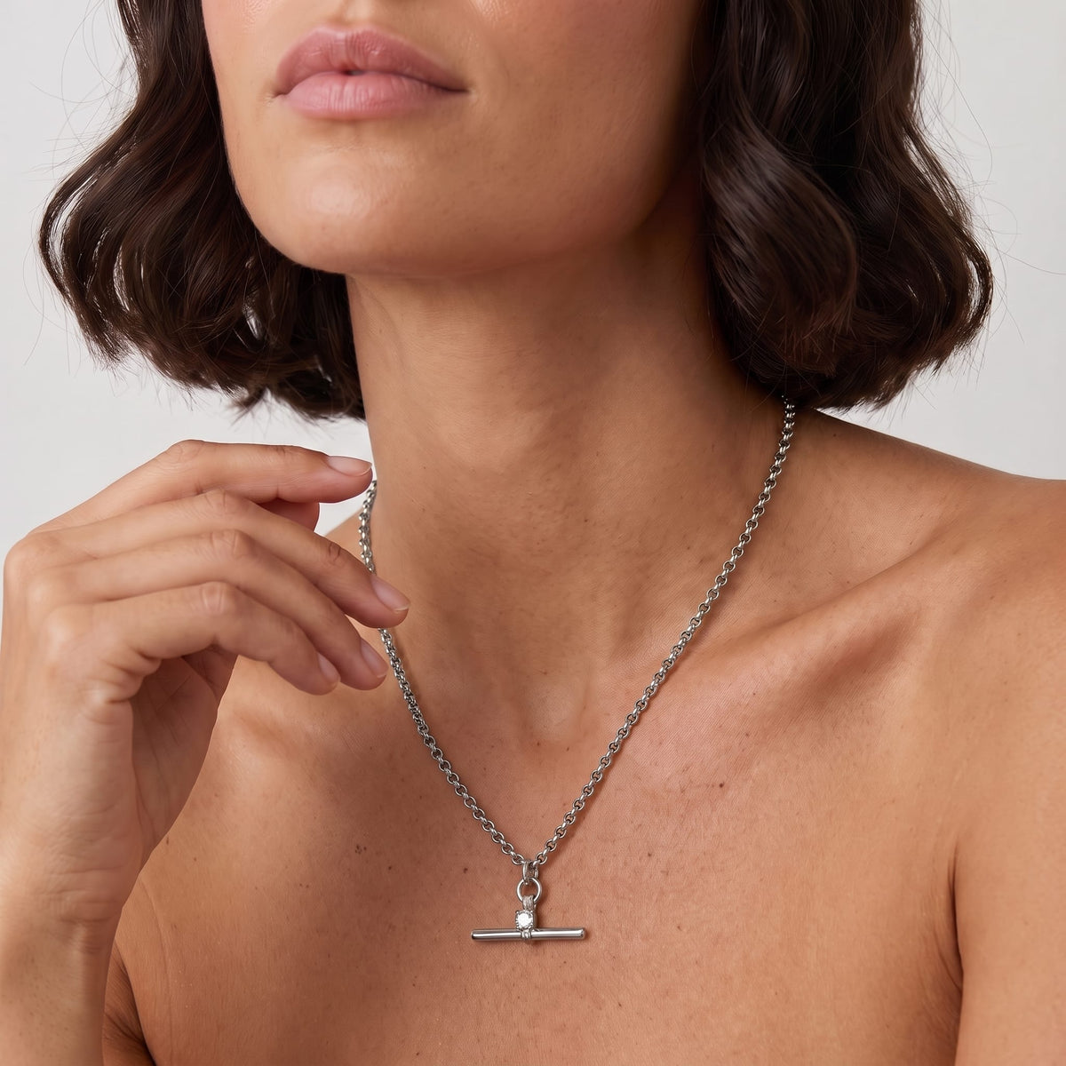 Woman wearing the Joséphine t-bar crystal silver necklace at the collarbone with hand near jaw