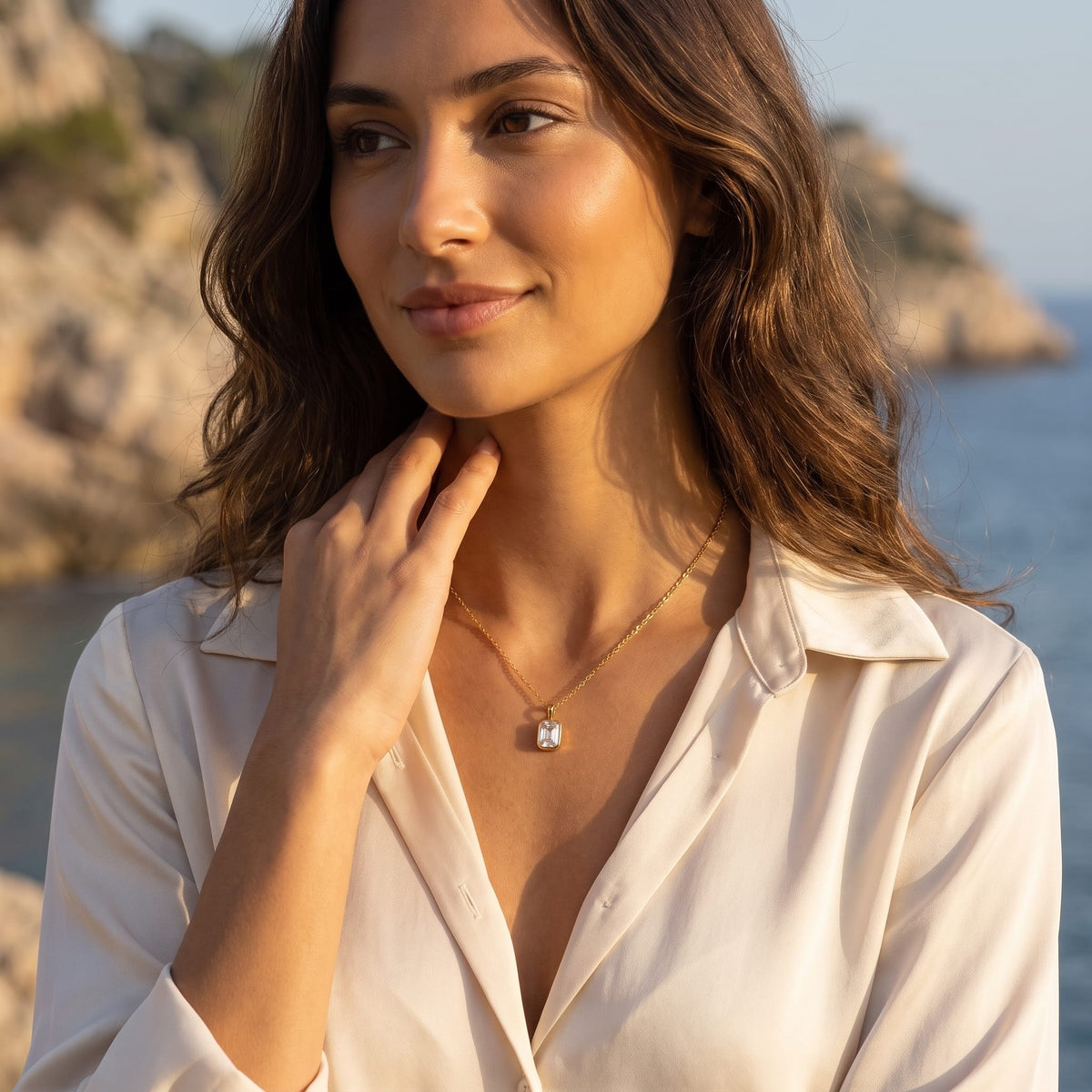 Woman wearing the Livia emerald-cut solitaire gold necklace at the collarbone outdoors in sunlight