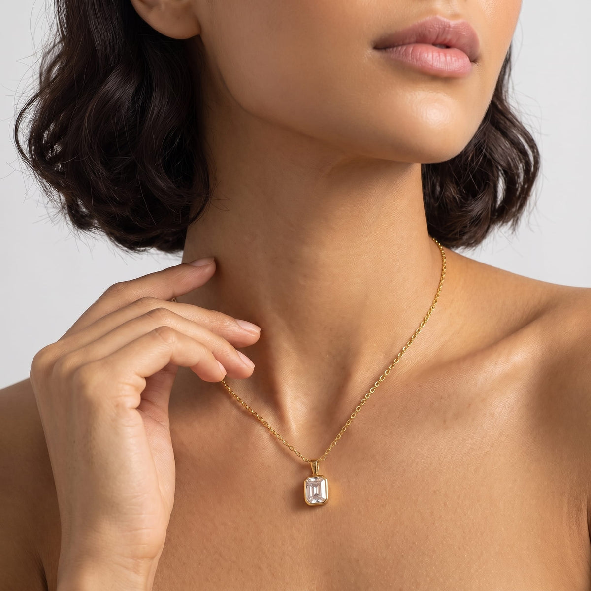 Woman wearing the Livia emerald-cut solitaire gold necklace at the collarbone touching her neck