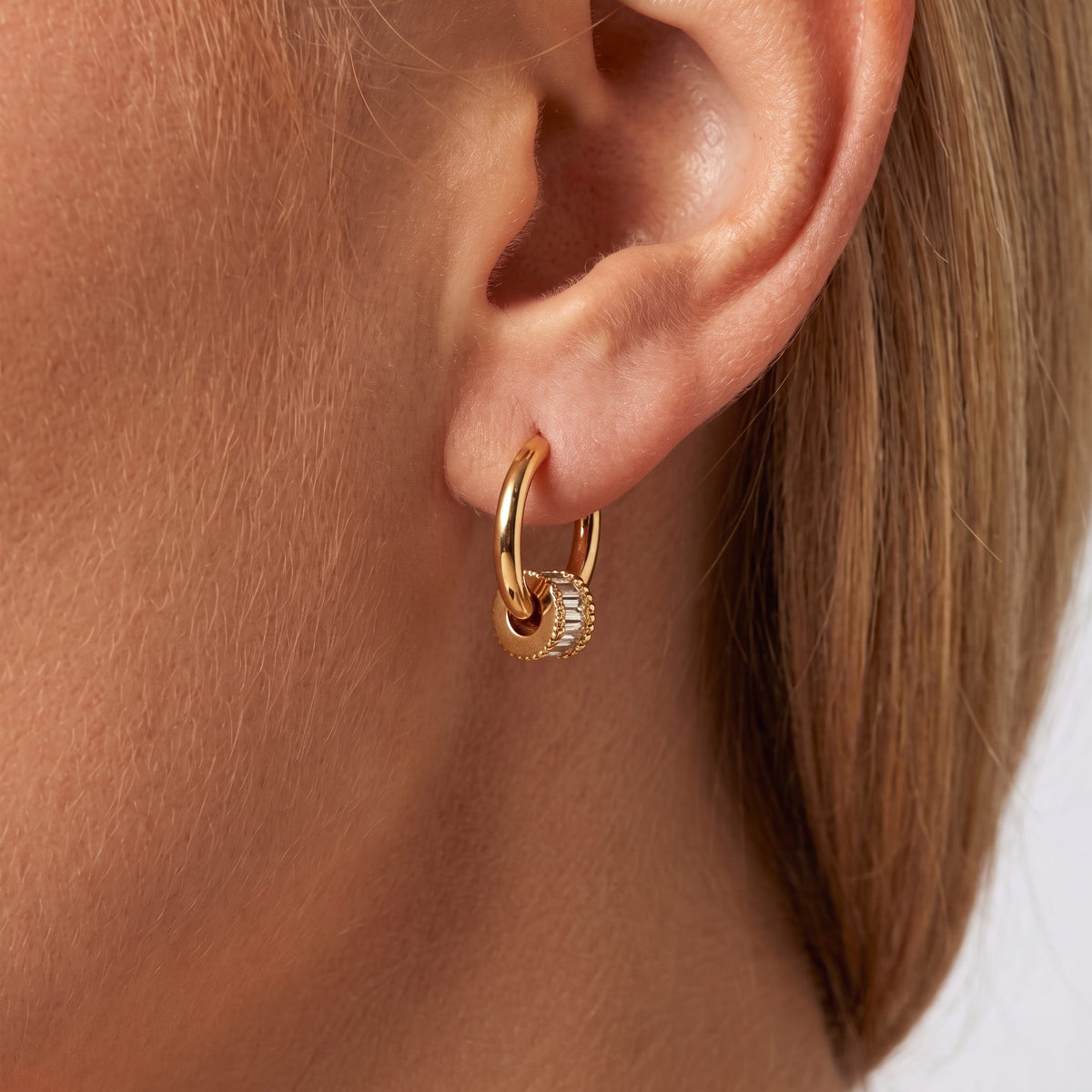 Woman wearing the Maia crystal earring, a gold hoop threaded with a ring of baguette crystals