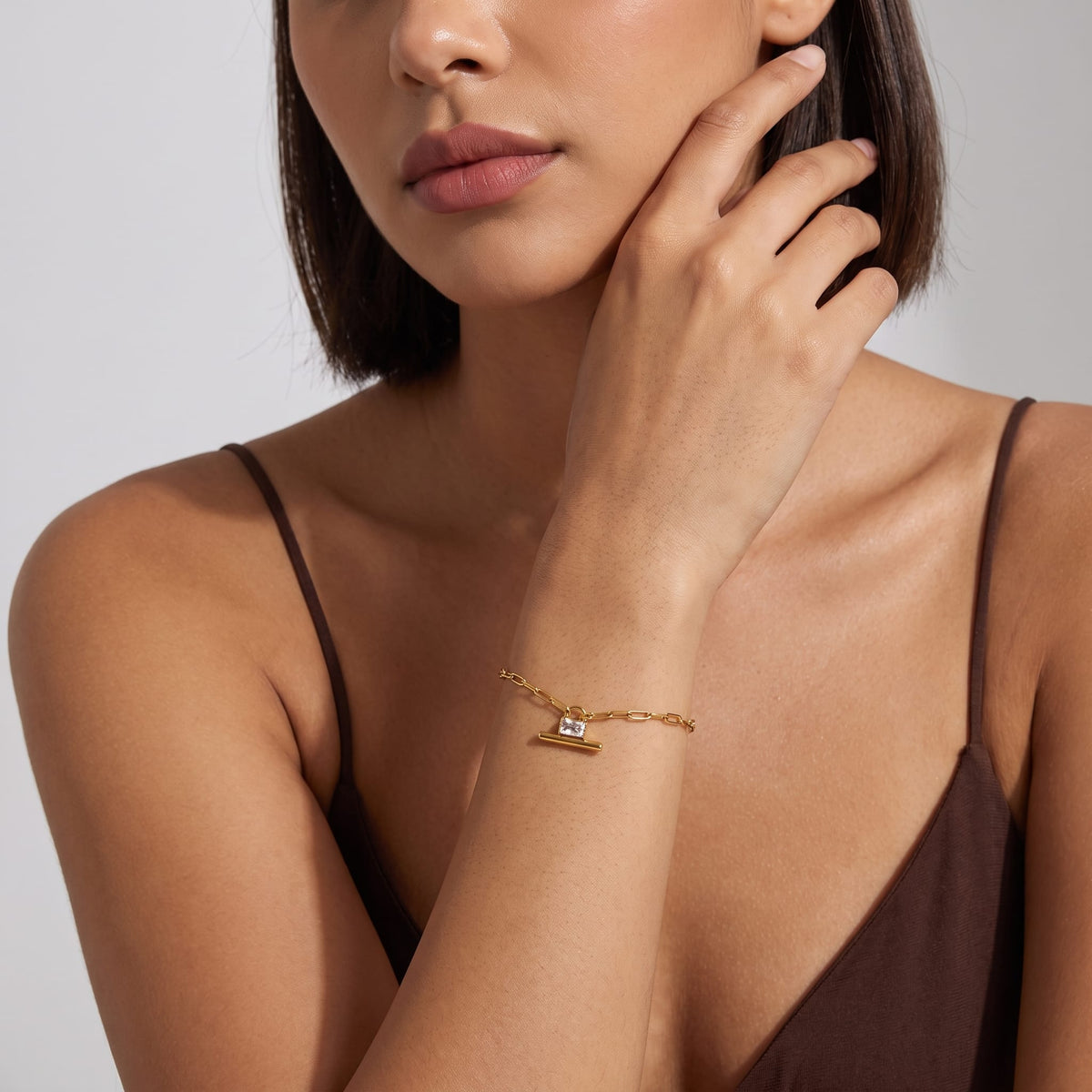 Woman wearing the Margaux padlock t-bar gold bracelet on her wrist wearing a brown tank