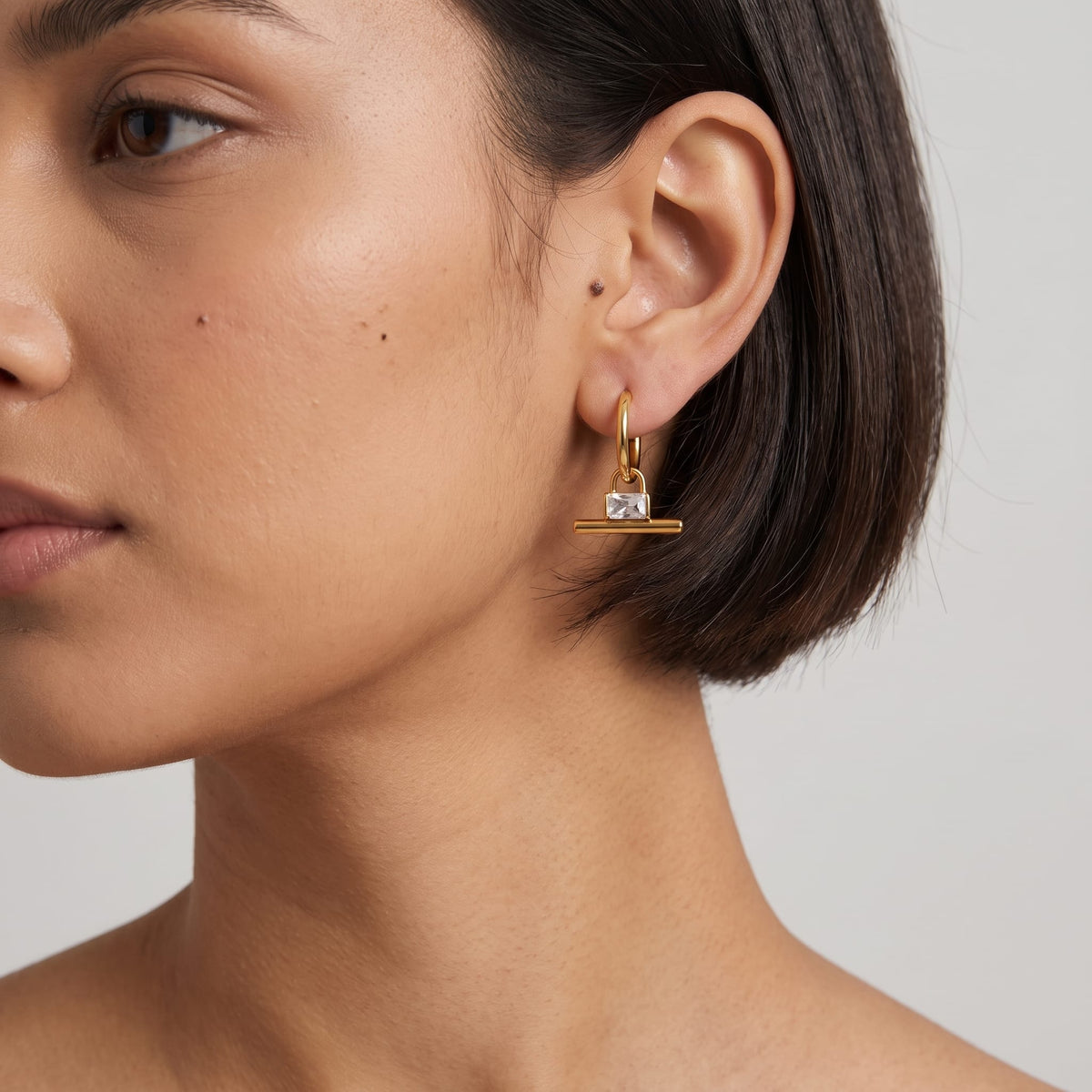 Woman wearing the Margaux padlock t-bar gold earrings on her ear with short dark hair
