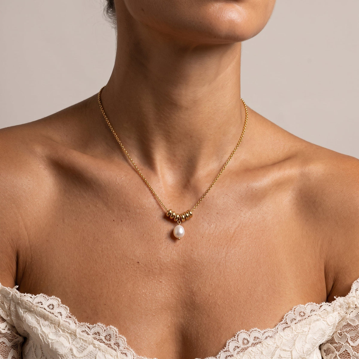 Wider view of a woman wearing the Mathilde pearl drop gold necklace at the collarbone