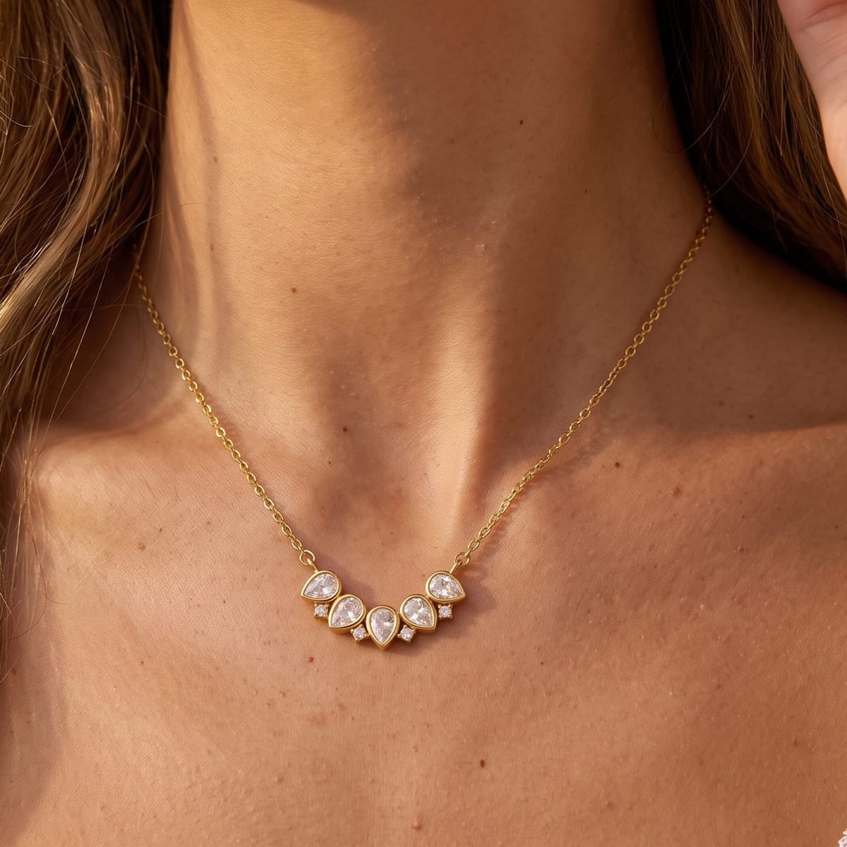 Woman wearing the Mélisande crystal crescent gold necklace at her collarbone with hand near hair