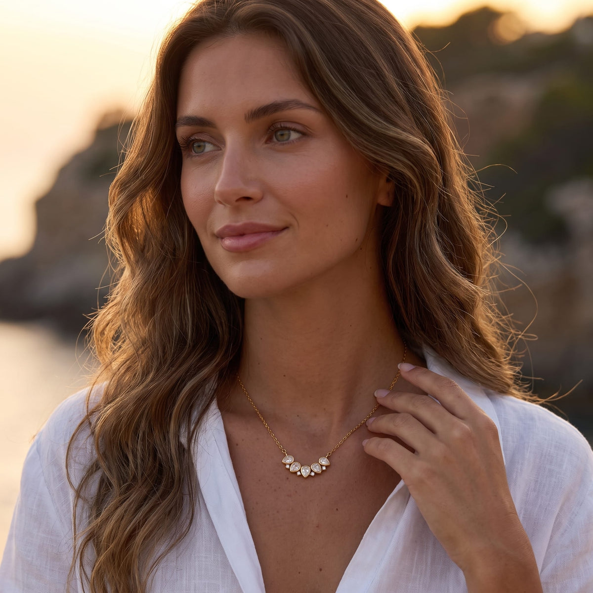 Woman wearing the Mélisande crystal crescent gold necklace at her collarbone outdoors in white shirt