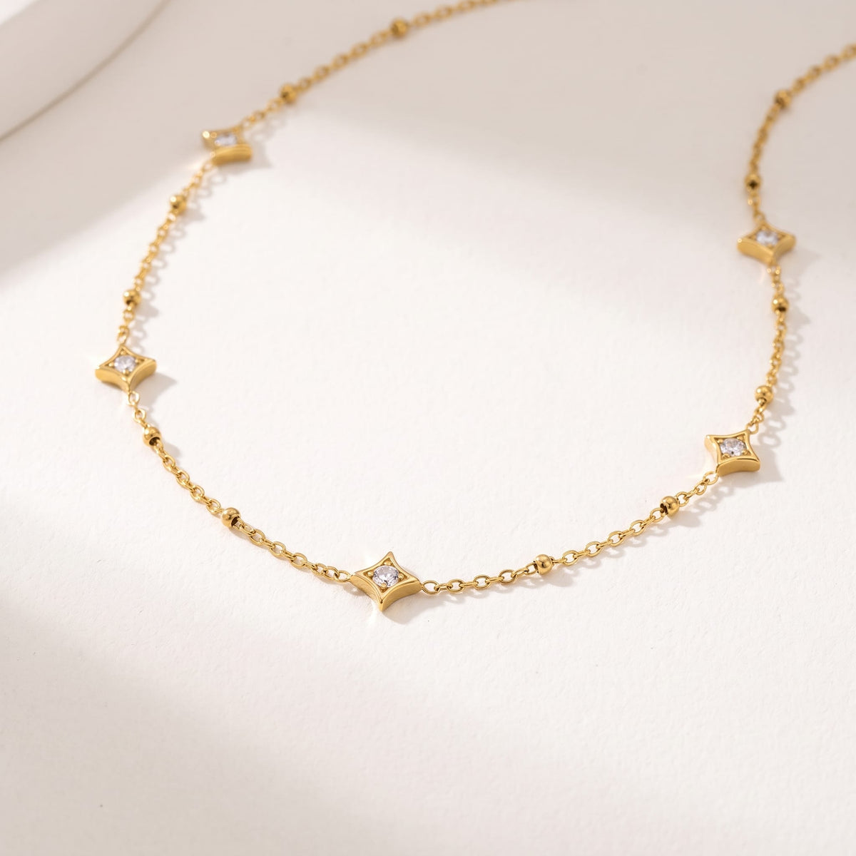 Océane star station gold necklace on a white surface with soft diagonal shadows
