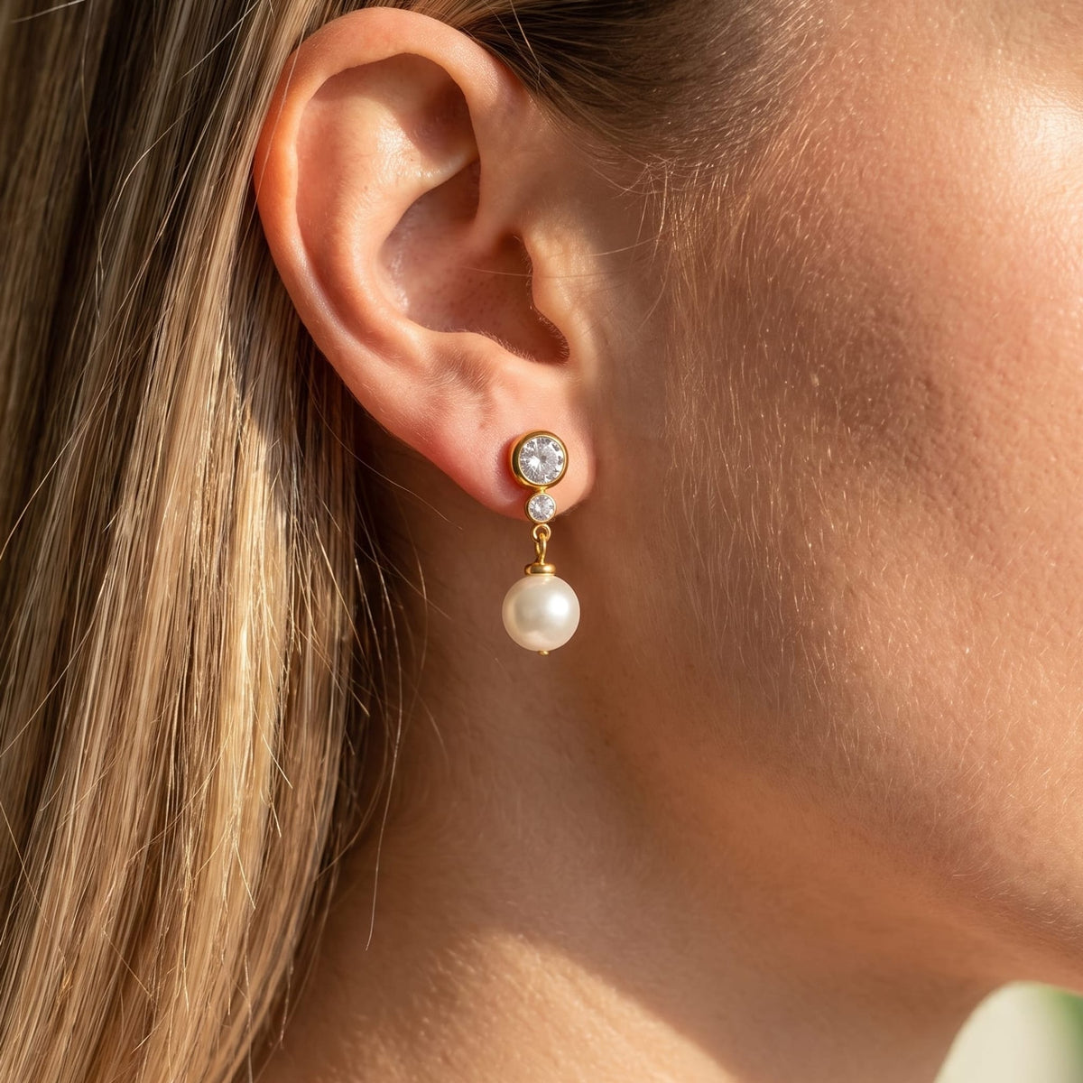 Woman wearing the Odette crystal pearl gold earrings on her earlobe in sunlight