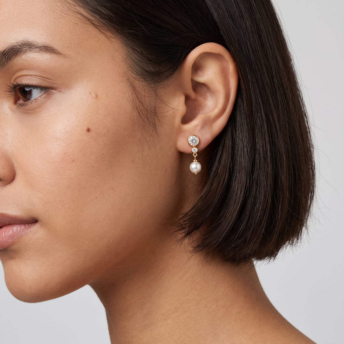 Woman wearing the Odette crystal pearl gold earrings on her earlobe with short dark hair